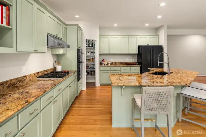 Thoughtfully remodeled kitchen featuring a Wolf gas stovetop and Viking hood, freshly painted cabinets, granite slab countertops, pantry, and island with seating.