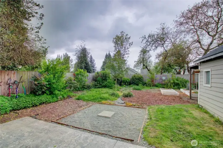 Fenced backyard, concrete patio, firepit area, lots of native plants and raised beds.