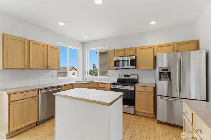 A large grouping of corner windows bring this kitchen joyful light. Featuring long counters, large cabinets, stainless appliances and a center island with a butcher block top, this is a kitchen roomy enough for even multiple cooks.