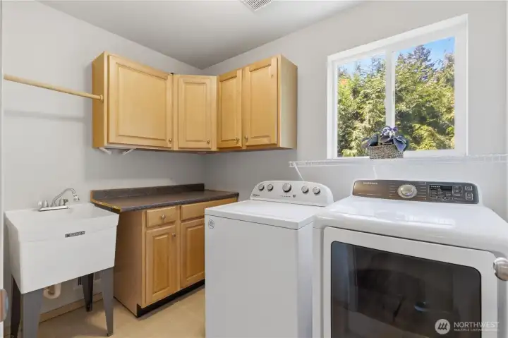 Bright and functional upstairs laundry room designed for convenience, complete with a deep utility sink, abundant cabinet storage, and a folding counter. Space for a side-by-side washer and dryer, plus a large window that brings in plenty of natural light, makes laundry day a little more enjoyable.