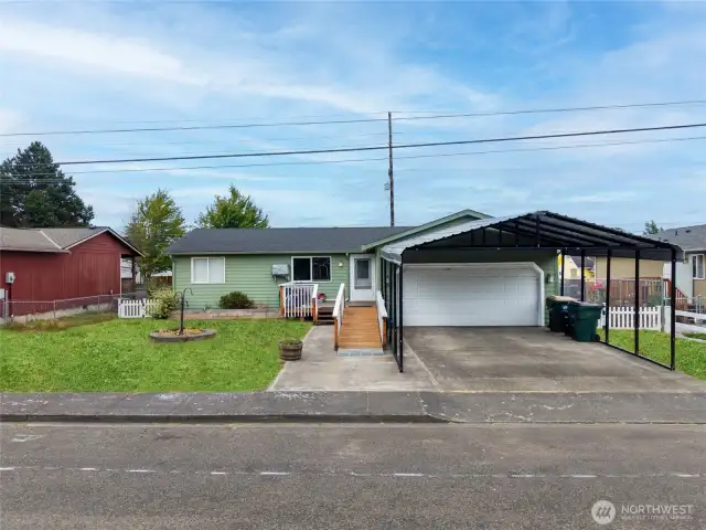 The practical metal carport stays with the home and, in combination with the garage, provides 4 covered parking spaces. May work for small RV. Photo edited grass.