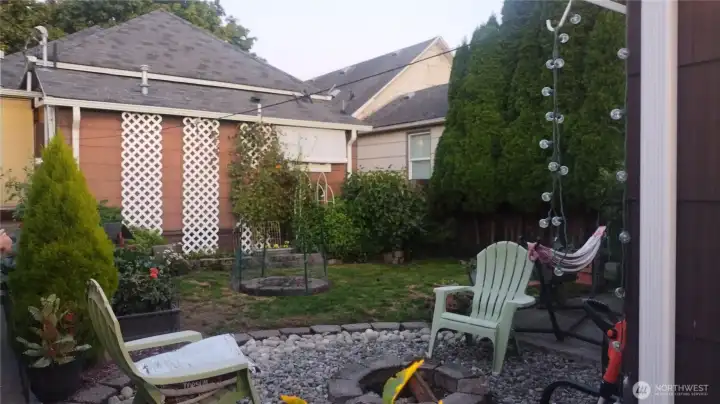 Another view of the backyard with lawn in the middle, fire pit and mature landscaping.  The path to the back house door is on the left.