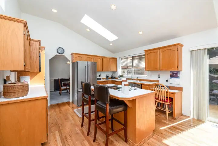 This spacious kitchen features, warm-toned cabinetry, stainless steel appliances, skylight, and designated desk for household management.