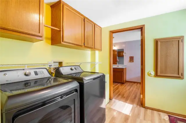 The laundry room area is right by the back door and has a couple shelves, a place to hang clothes and several cupboards for storage. The beautiful washer and dryer go with the home. The primary bathroom is through that doorway, and the back door is on the right.