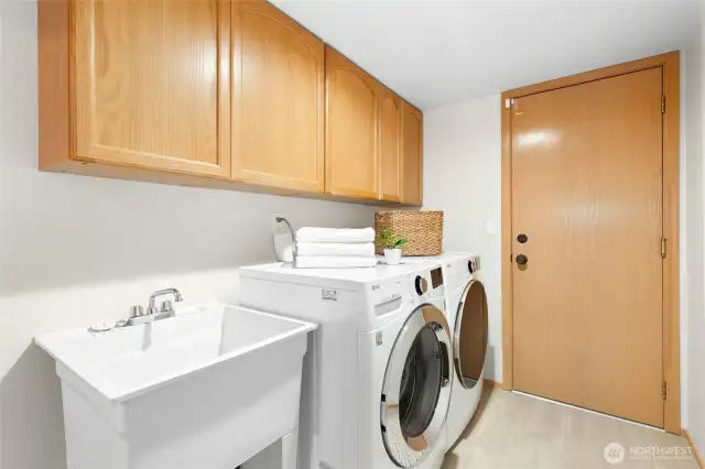 Utility room with cabinets, sink and door leading out to the garage.