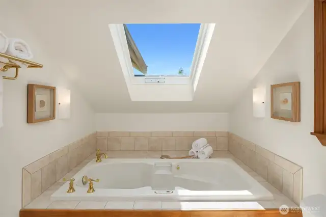Spa-like primary bathroom with tub and skylight.