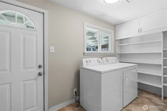 Dedicated laundry room with built-in shelves, a large storage cabinet, and natural light from the window.