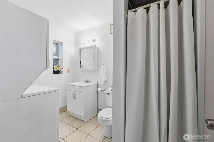 Functional ADU bath with tile flooring and stacked washer and dryer.