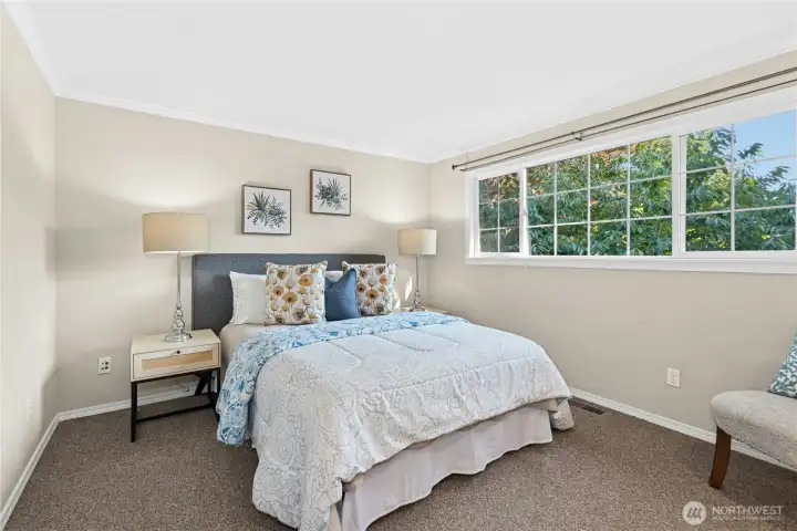 Primary suite with carpeted floor and large window overlooking the backyard is a peaceful retreat in this Kirkland home.