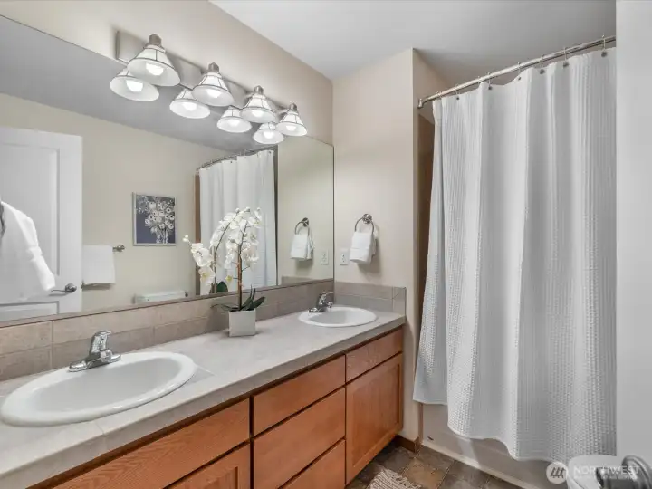 Full size bathroom with double vanities and large wall to wall mirror and clean shower/tube combo.