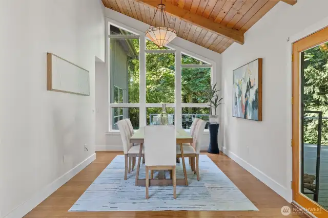 Framed by dramatic windows and surrounded by greenery, the dining room offers a peaceful setting for gatherings.