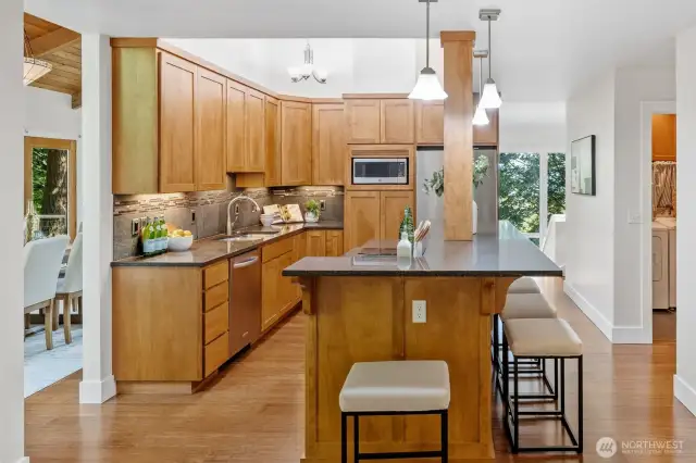 Warm wood cabinetry, granite countertops, and under-cabinet lighting create a welcoming and functional kitchen space with a direct line of sight to the dining area.