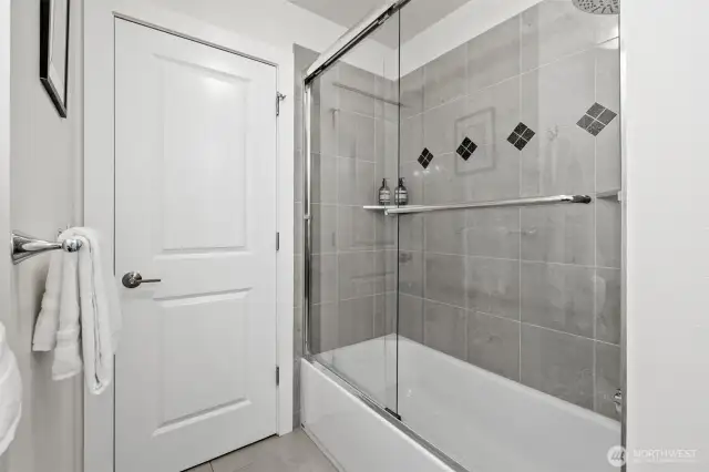 A tiled shower-tub combo with glass enclosure and accent detailing completes the full main-level bath—perfect for guests or everyday use.