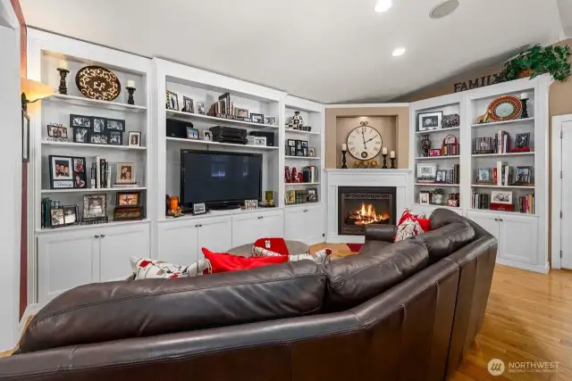 The family area with hardwood flooring and vaulted ceiling adds to the open concept feeling complete with custom floor to ceiling built-ins and a cozy gas fireplace