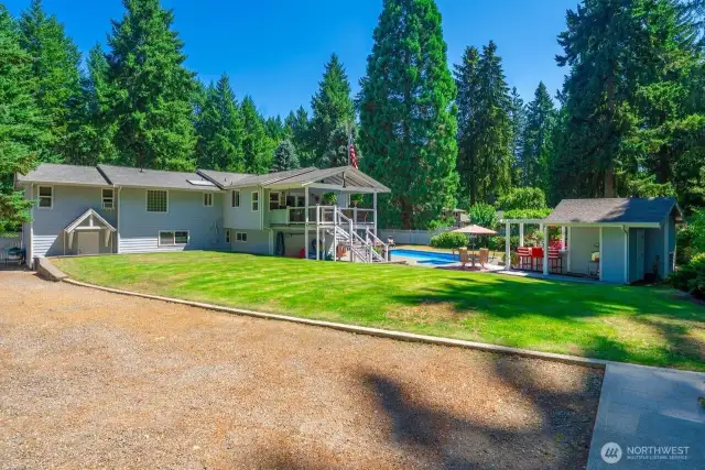 This is a view from the shop area looking toward the house with wide parking area and the back drop of trees, there's also RV Parking a with designated plug in.