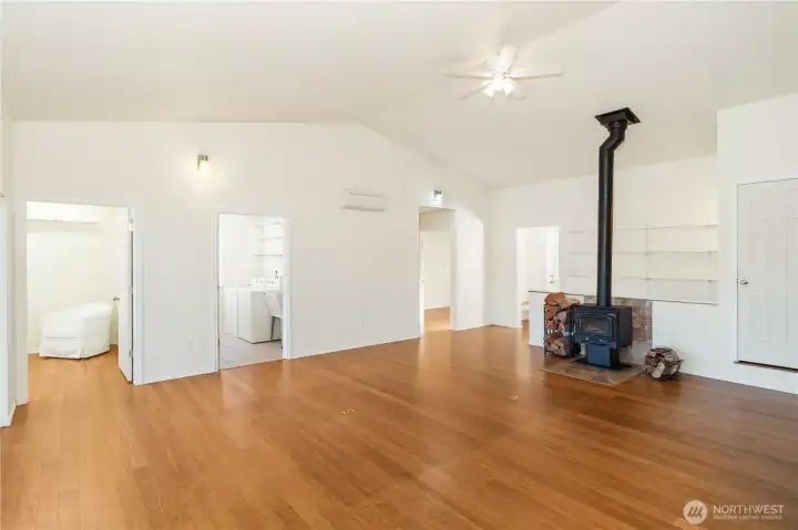 Enjoy open floor plan w/ vaulted ceilings and plenty of natural light. Office is shown on the left (with white chair), laundry, guest bedroom and door to entry. Stairs are behind wood burning stove.
