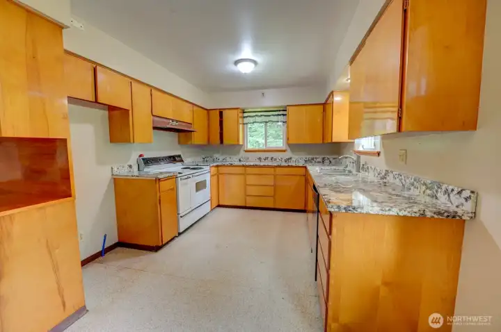 Kitchen with updated counter tops, vintage stove/range and black dishwasher across the kitchen. Sink is located next to the dishwasher. Refrigerator cutout space in cabinetry next to the stove.