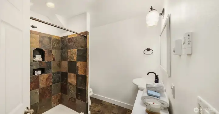 Lower level- a striking three-quarter bathroom with heated tile floors, dedicated thermostat, and slate shower surround.