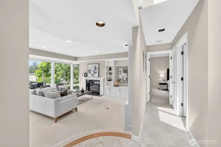 From the moment you step inside, the home opens into a sweeping neutral palette that Six Walls Interior Design executed with intention — warm greige walls, new recessed lighting, and a gas fireplace flanked by custom built-ins that anchor the room. The curved staircase detail in the foreground and the hallway leading to the bedroom wing speak to a floor plan that flows effortlessly between living and private spaces. Everything you see — walls, floors, lighting, millwork — was rebuilt new in 2017.