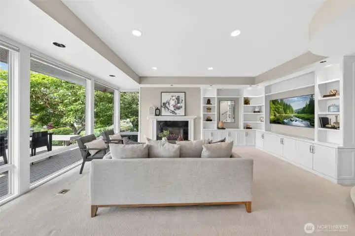 The custom built-in cabinetry wall is the design centerpiece of the main living area — floor-to-ceiling shelving, lower cabinet storage, and a perfectly proportioned fireplace surround, all finished in crisp white against warm neutral walls. New recessed lighting washes the space evenly while oversized windows flood the room with natural light and treetop green. This is a room designed for real life — equally at home hosting a dinner party or a quiet Sunday morning.