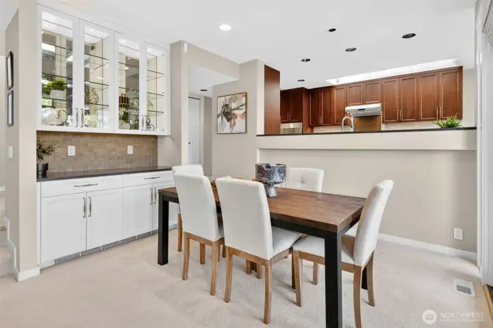 The dining room earns its place with a custom built-in hutch featuring glass-front uppers, mirrored shelving, and designer tile backsplash — a butler's pantry moment that makes entertaining feel considered rather than improvised. The kitchen pass-through keeps the cook connected to the table without sacrificing the intimacy of a defined dining space.