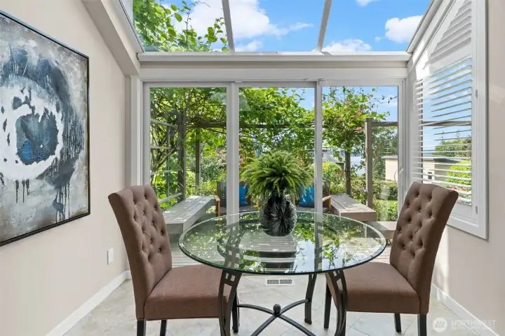 Tucked at the end of the kitchen, this sun-drenched breakfast nook is the home's best-kept secret — a glass ceiling canopied by a climbing vine pergola, with Lake Washington glinting through the garden just beyond the slider. Plantation shutters and tile floors complete a space that feels like a private conservatory steps from your stovetop.