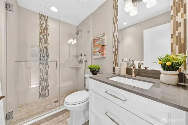 The main level bath delivers full design intention — mosaic glass accent tile, frameless glass shower, quartz vanity, and undermount sink, all installed new in the 2017 renovation. A guest bath that feels anything but.