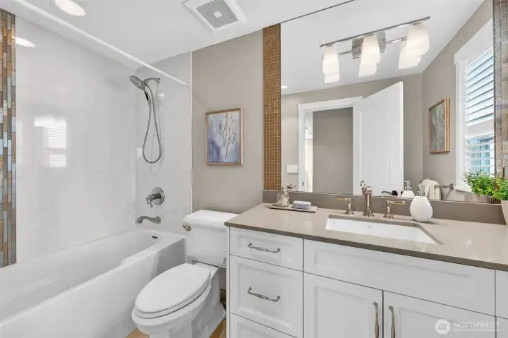 Upper Level Full Bath features marble-surround tub and shower, mosaic glass accent tile, quartz vanity, and polished nickel fixtures — the upper level bath received the same design attention as every other room in this renovation. Plantation shutters and a well-placed mirror keep the space feeling bright and considered rather than purely functional.