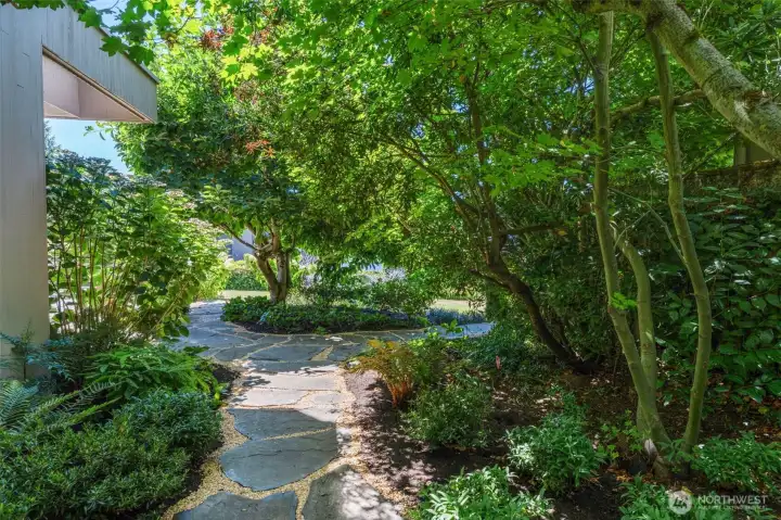 A meandering flagstone path winds through the well-designed garden beneath a canopy of mature Japanese maples and specimen trees — the kind of grounds that take decades to establish and can't be replicated by a renovation budget alone.
