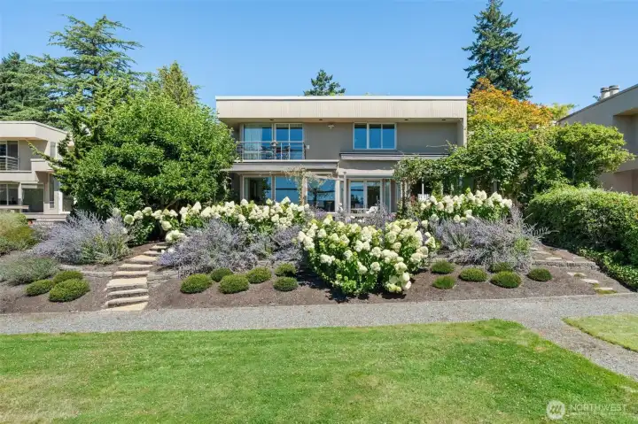 The full rear elevation reveals the true scale of this outdoor living space — the primary suite balcony above, the main level deck below, the glass breakfast room conservatory to the right, and Ohashi's sweeping garden beds tying it all together in a setting that is unmistakably Lochleven.