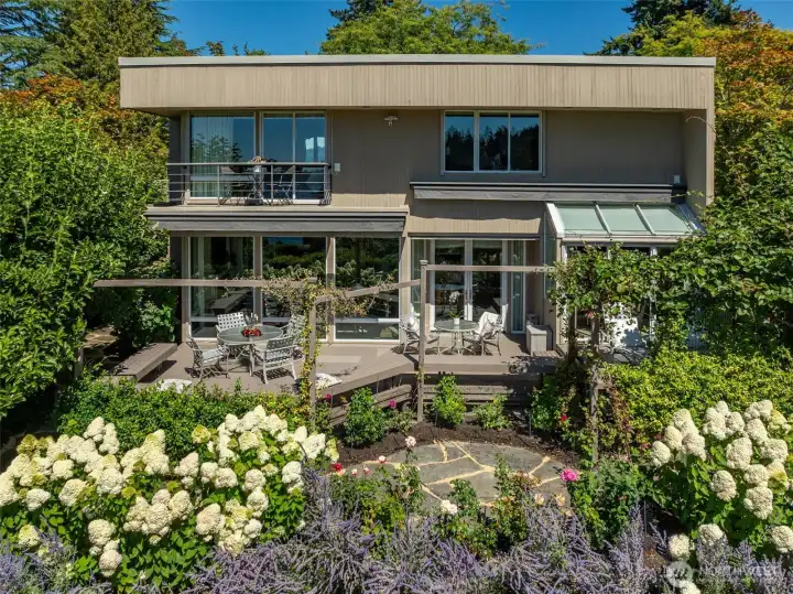 From above, the Ohashi landscape design tells its full story — sweeping beds of hydrangeas, lavender, and roses framing the new deck, flagstone paths threading through mature plantings, and the primary suite balcony commanding the view above it all. This is the garden that turns a great house into an extraordinary home.