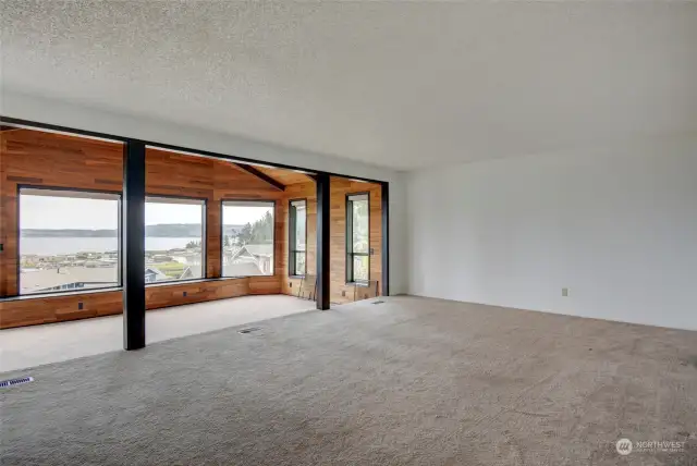 Spacious living room that steps down to a wood paneled indoor porch-like area with views to the water and mountains.