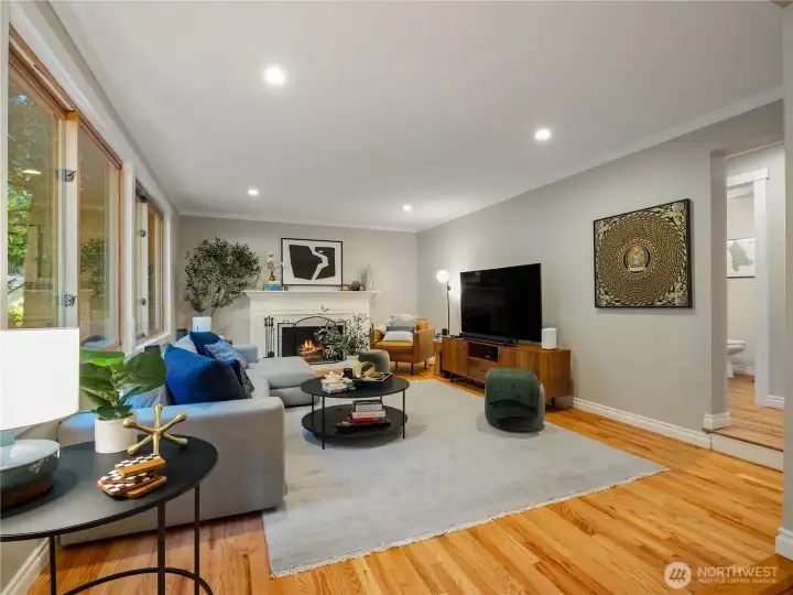 The kitchen flows directly into the bonus/great room — a warm, inviting space anchored by a classic fireplace, beautifully framed by more wood-wrapped windows, and opens to the expansive back deck & private gardens.