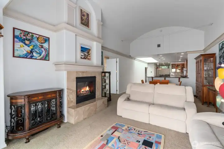 An open view into the living room, with the primary suite to the left and the kitchen beyond, creating an easy, flowing layout. In this photo you can see the tall, vaulted ceilings and skylight which creates a light filled and expansive space for entertaining.