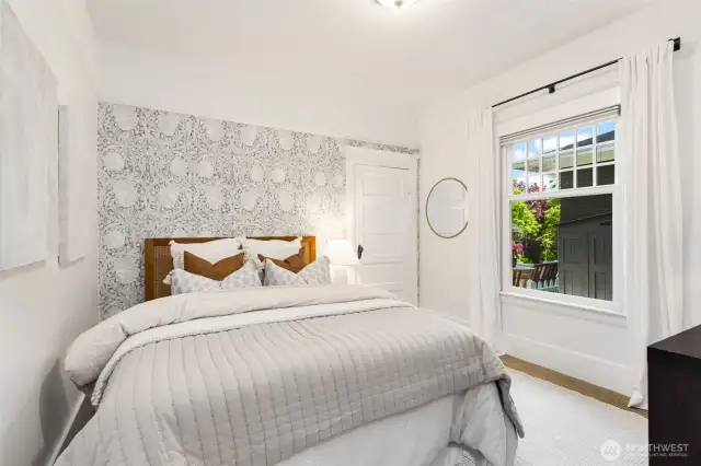 The main floor bedroom features beautiful wallpaper accent and a window to the side yard.  The door goes to a large walk-in closet.