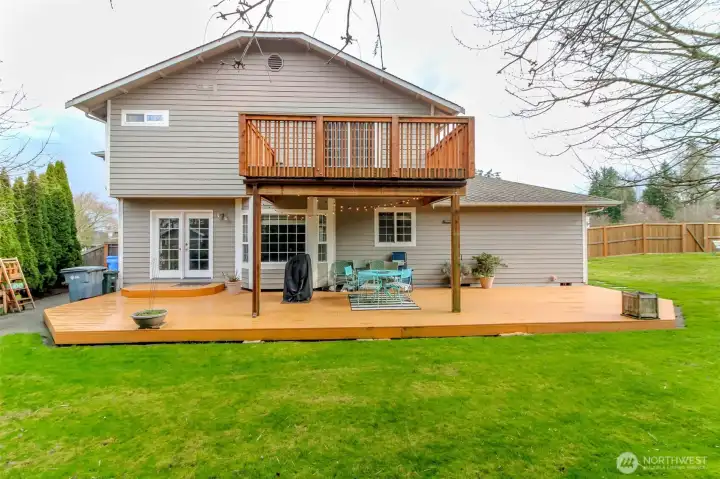 A rear facing view of this beautiful home with a sprawling, expansive backyard that feels private and inviting. The backyard is fully fenced, ensuring a safe , secluded outdoor space. A large deck on the main floor extends from the back of the home, perfect for outdoor dining and entertaining, while a generous sized deck extends off the primary bedroom upstairs. The landscape features lush mature greenery adding to the sense of privacy.