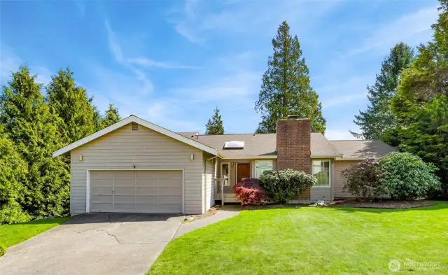 Contemporary Northwest-style residence with horizontal lap siding, prominent brick chimney, and a streamlined two-car garage. Framed by mature evergreens and manicured plantings, the façade sets a serene and polished tone for the rest of the home.