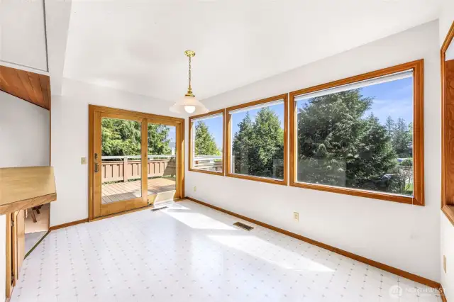 The dining area is surrounded by picture windows and sliding doors that lead to the deck. A pendant light adds charm to this airy, sun-filled space perfect for meals or gatherings.