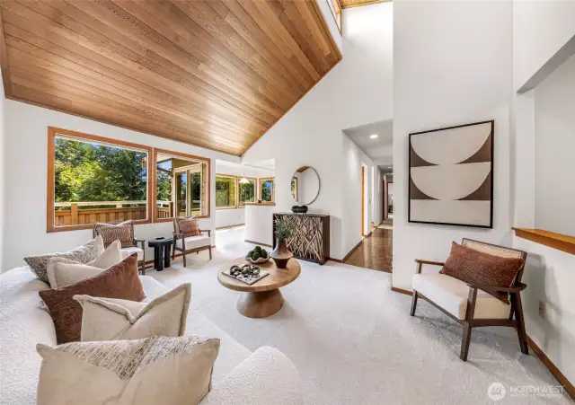 Expansive living area with tongue-and-groove cedar ceiling, oversized windows, and seamless indoor-outdoor flow to the deck. The neutral palette and organic textures complement forest views, creating a serene and elevated Northwest aesthetic.