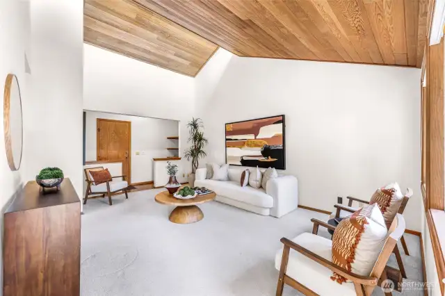 Spacious living room features vaulted cedar ceilings, large windows, and soft carpeting for cozy comfort. A neutral palette and thoughtful staging highlight its welcoming ambiance.
