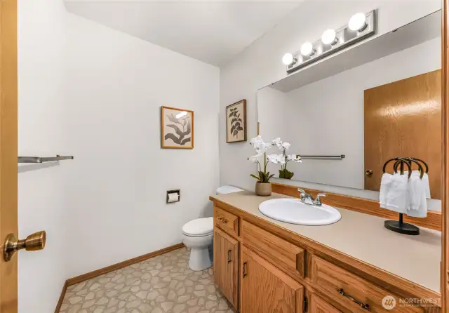 Convenient half bath on the main floor includes a wide vanity with oak cabinetry, large mirror, and decorative lighting. Ideal for guests and day-to-day use.