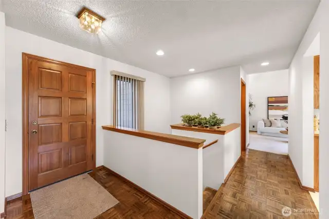 Upper hallway view toward the front door showcases parquet flooring and recessed lighting. A crisp, clean entry impression sets the tone for the home.