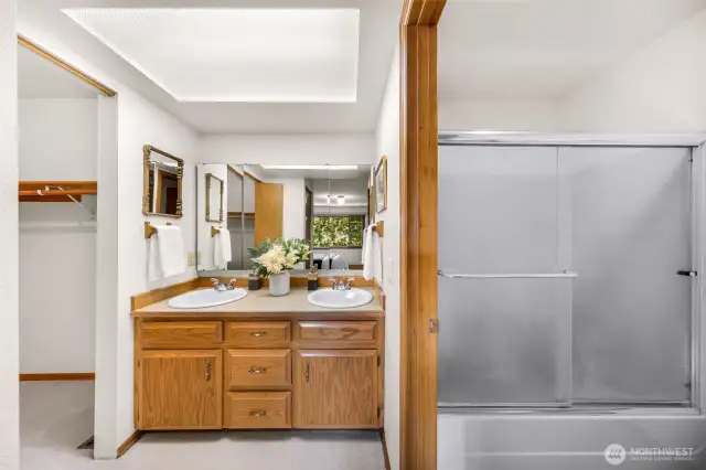 Ensuite bath includes a double-sink vanity, mirrored wall, and built-in storage. Soft lighting and oak cabinetry make this a serene and functional space.