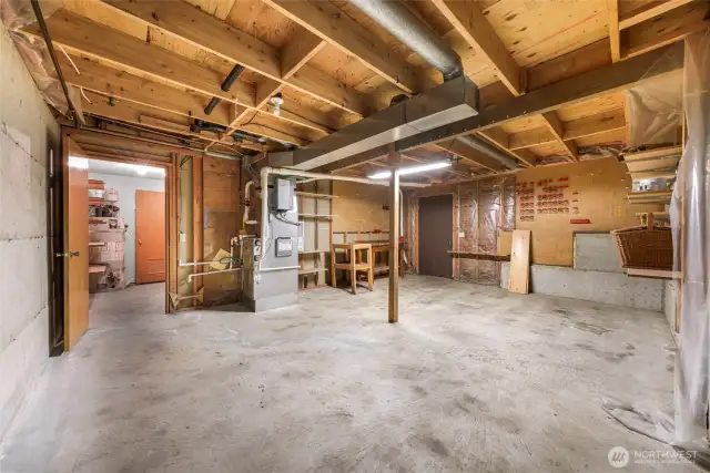 The unfinished utility area includes workspace, exposed beams, furnace, and extensive shelving—ideal for projects, storage, or a workshop.