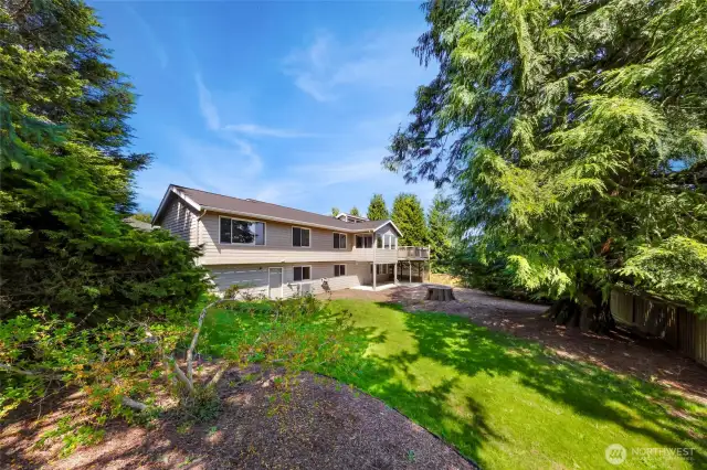 Angled rear view of the home showcases extensive lawn, mature trees, and private fencing surrounding the backyard.