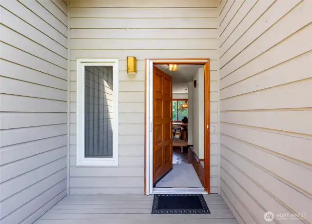 Covered front entry with wood-paneled siding and a warm wood front door offers a welcoming first impression, enhanced by a modern exterior light fixture and clean-lined trim.