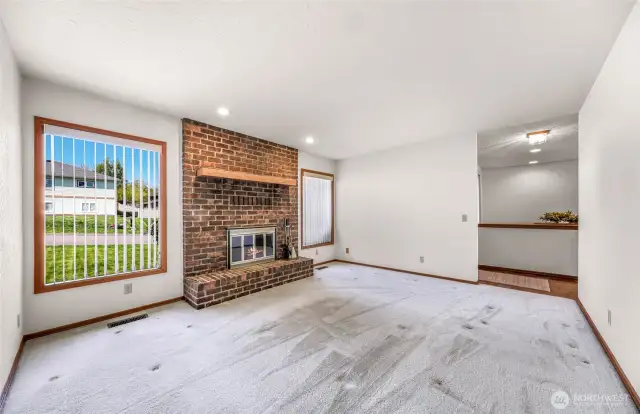Another angle of the inviting living room highlights the open layout and natural light from dual windows, showcasing a well-maintained brick hearth and neutral carpet ready for personalization.