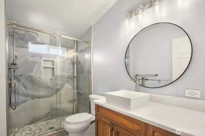 Spa-Inspired Bathroom with a Frameless Glass Walk-in Shower, Striking Marble tile, Rainfall Shower Head with Handheld Sprayer, Quartz Counters, Vessel Sink, Designer Lighting, and a Rich Wood Vanity that adds Warmth and Sophistication