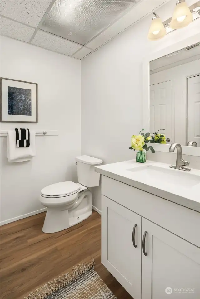 The lower level powder room with a new cabinet, quartz counter, sink, faucet, mirror and lighting.