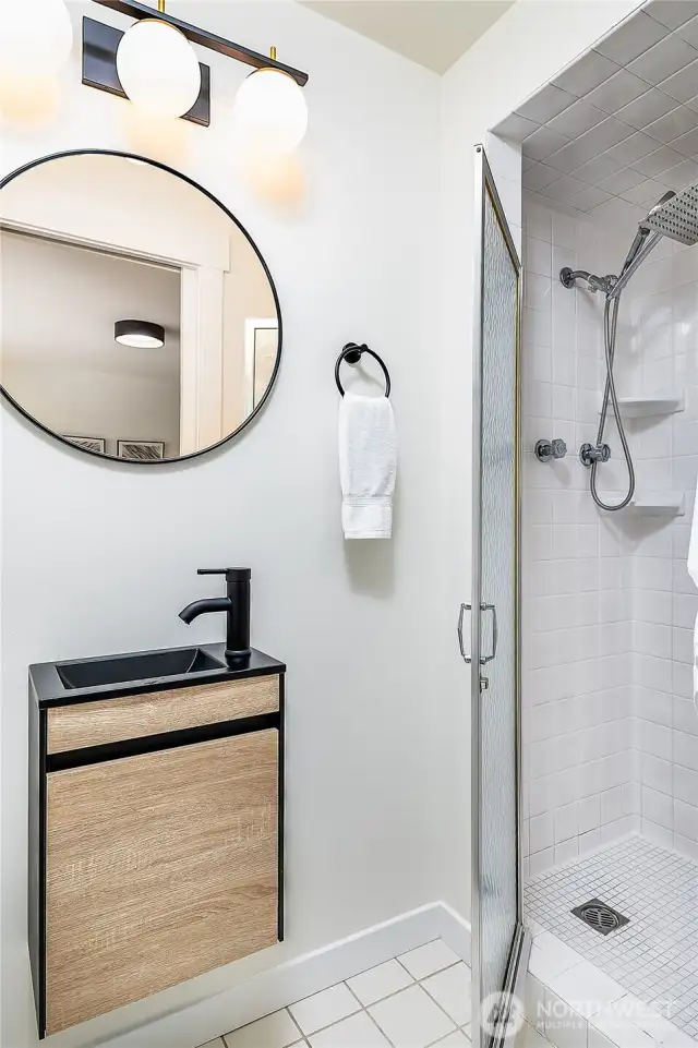 Primary ¾ bath designed for efficient use of space, featuring a charming compact sink on the left and a spacious shower on the right.